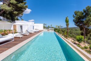 Luxury villa pool area with chairs and beds, offering stunning sea and mountain views in Es Cubells, Ibiza.
