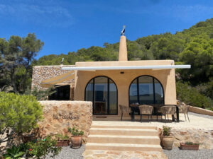 Exterior view of a stunning 3-bedroom villa with 180-degree panoramic views of Cala San Vicente valley, showcasing its natural stone cladding, lush greenery, and peaceful hillside setting.