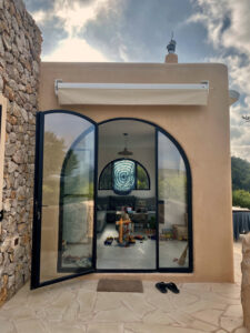 Exterior view of a stunning 3-bedroom villa with 180-degree panoramic views of Cala San Vicente valley, showcasing its natural stone cladding, lush greenery, and peaceful hillside setting.