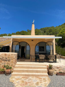 Exterior view of a stunning 3-bedroom villa with 180-degree panoramic views of Cala San Vicente valley, showcasing its natural stone cladding, lush greenery, and peaceful hillside setting.