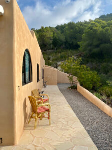 Exterior view of a stunning 3-bedroom villa with 180-degree panoramic views of Cala San Vicente valley, showcasing its natural stone cladding, lush greenery, and peaceful hillside setting.