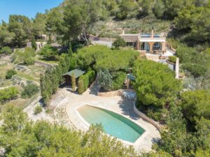 Aerial view of Cana Pedrera: a luxurious villa in Ibiza with a pool, garden and stunning landscapes, captured from a drone.