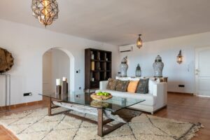 Spacious living room at Luxury Casa Flamenc, Ibiza, featuring a cozy sofa, center table, panoramic window with pool view, and staircase to the second level.