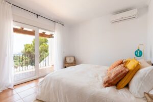Elegant master bedroom at Luxury Casa Flamenc, Ibiza, featuring a king-size bed and a window offering panoramic views of the surrounding landscape.