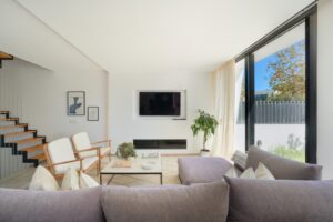 Spacious living room in Luxury Villa Jesús, Ibiza, featuring comfortable furniture, a center table, TV, panoramic window with garden view, and a staircase leading to the upper floor.